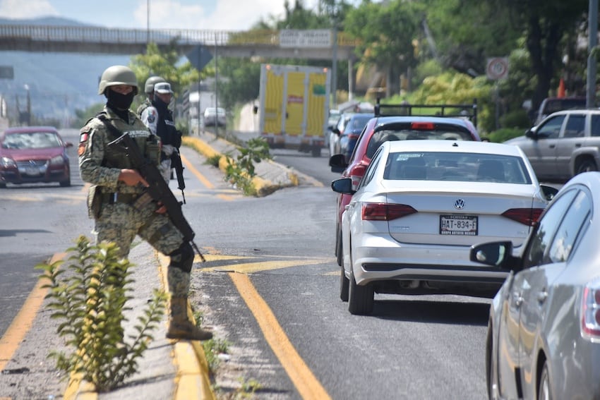 Armed security forces stand guard next to a busy highway